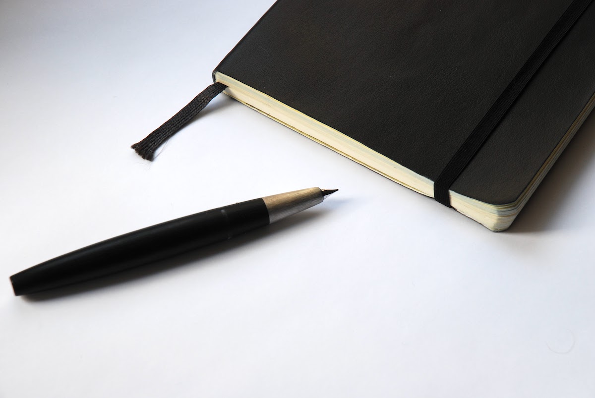 A black Moleskine notebook and fountain pen on a white surface